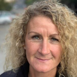 Llun o Lisa, dynes wen gyda gwallt cyrliog golau, yn gwenu ar y camera.