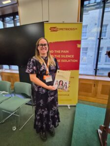 A picture of Lowri in a long floral dress hold a copy of the report and wearing an FTWW lanyard.